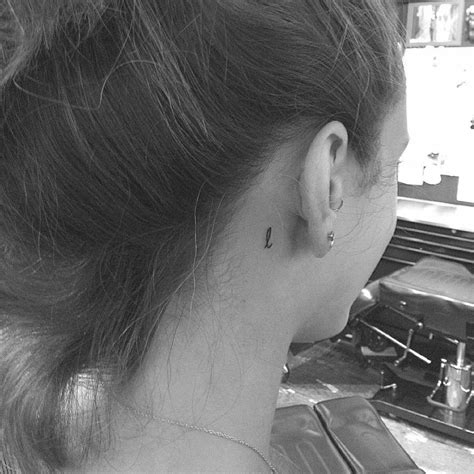 Minimalistic letter "L" tattoo located behind the ear.
