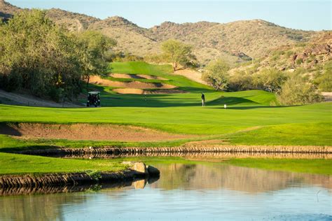 a golf course with water in the foreground and mountains in the ...