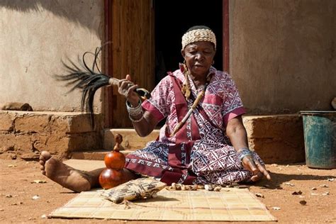 an old woman sitting on the ground with a bird in her hand and other items around her