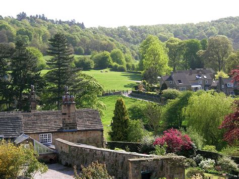 an old stone building in the middle of a lush green field with houses and trees