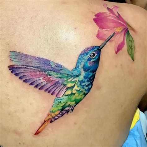a colorful hummingbird with a pink flower on its back side tattoo by the artist