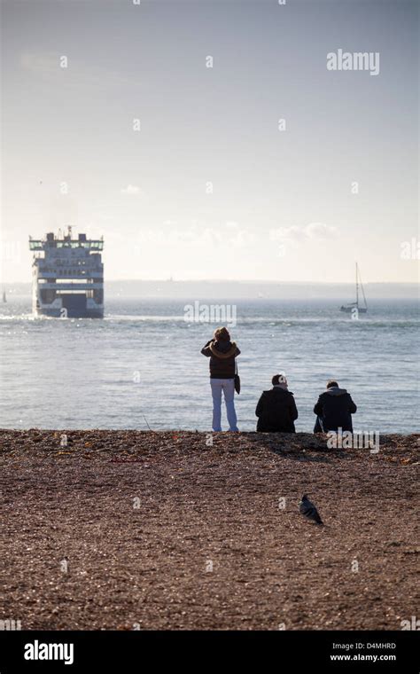 People on Southsea Beach in Portsmouth looking out to a Wightlink car ferry in the Solent ...