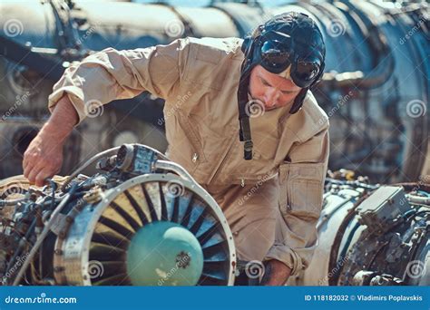 Portrait of a Mechanic in Uniform and Flying Helmet, Repairing the Dismantled Airplane Turbine ...