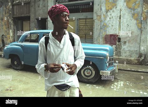 Cuban man smoking in a street in havana vieja with typical backdrop of classic 1950 s american ...