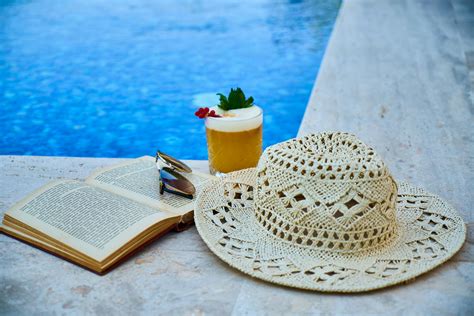 Beige Straw Hat, Book, Sunglasses, and Drink Beside Pool · Free Stock Photo