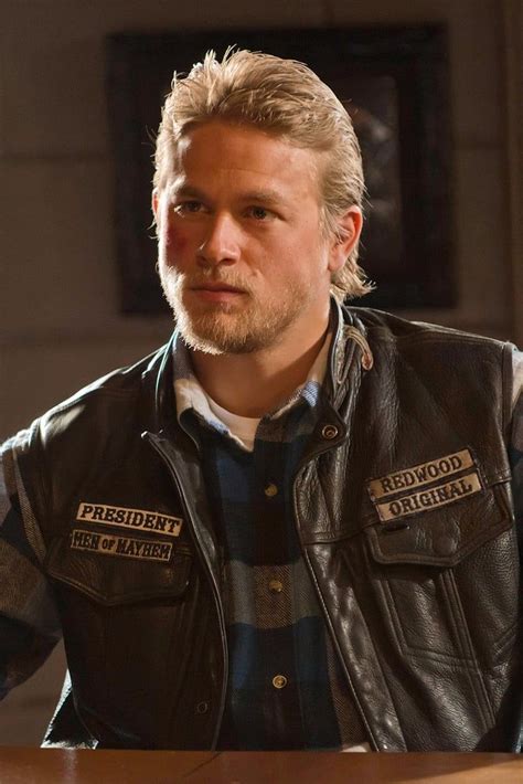 a man with blonde hair wearing a leather vest and looking off to the side while sitting at a table