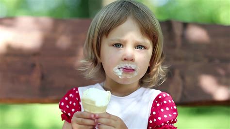 Beautiful girlie sits on the bench eats ice cream and licks her lips ...