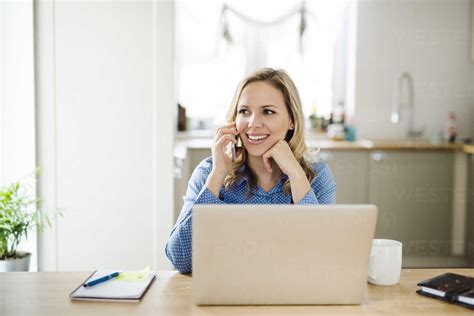 Smiling woman with laptop and cell phone working at home stock photo