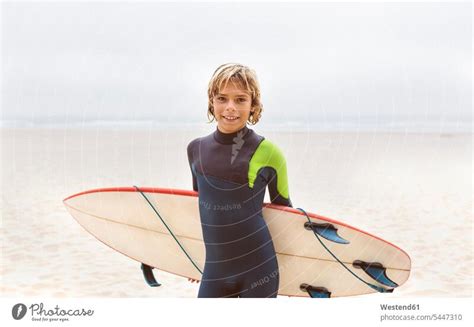 Spain, Aviles, portrait of smiling young surfer carrying surfboard on the beach - a Royalty Free ...