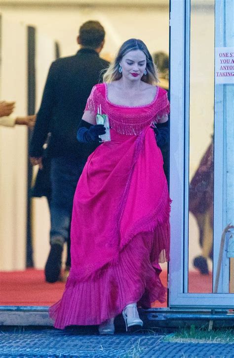 a woman in a long pink dress is walking out of a building with her hand on her hip