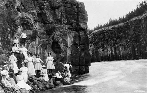 an old black and white photo of people standing on the side of a mountain stream