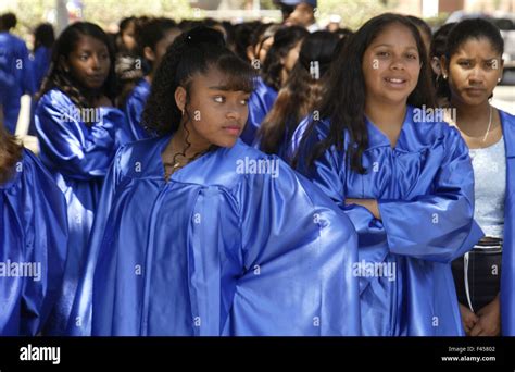 Hispanic and African American middle school girls wearing blue graduation gowns await ...