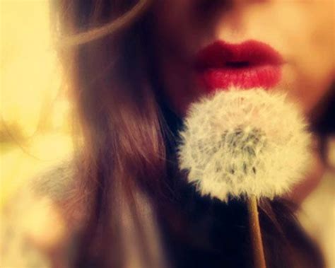 a woman holding a dandelion in front of her face with red lipstick on it