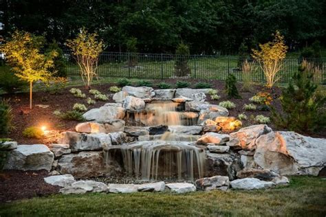 a small waterfall in the middle of a garden with lights on it's sides