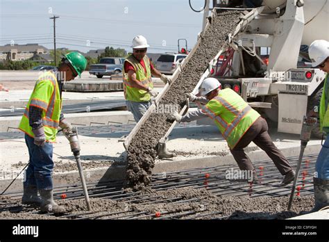 Male highway construction workers pour fresh concrete along new stretch of highway in Texas ...