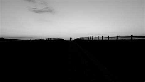 black and white silhouette shot of person walking on horizon with wooden fence, horizon person ...