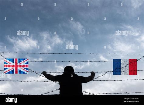 Man looking through barbed wire fence on beach flags of UK and France ...