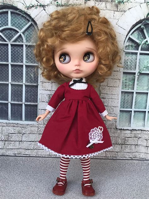 a doll is standing in front of a brick wall wearing a red dress and striped socks