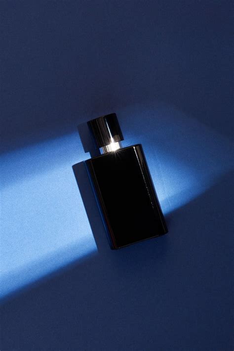 a black bottle with a light shining on it's side next to a blue wall