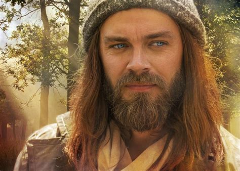 a man with long hair and a beard wearing a knitted hat is looking at the camera