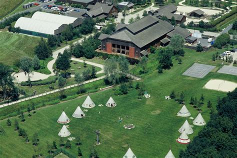 an aerial view of several tents in the grass near trees and buildings with tennis courts