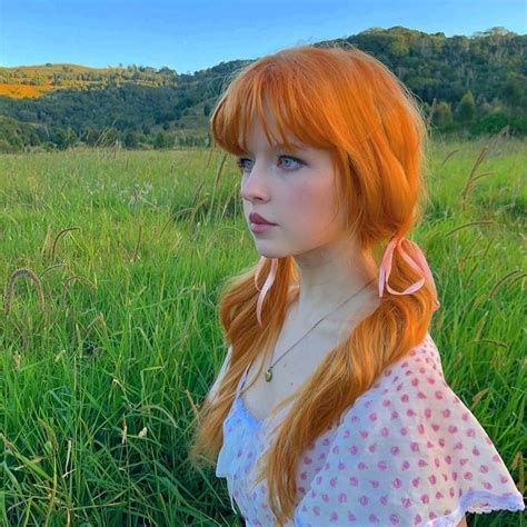 a girl with red hair is sitting in the grass and looking off into the distance