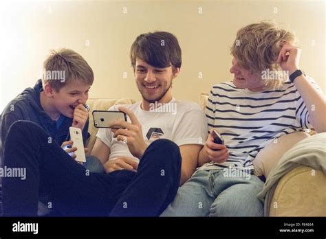 Three good-looking white happy teenage boys laughing and looking at their mobile phones playing ...