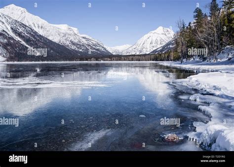 Montana Lake in Winter: Snow covered mountains reflect from the icy surface of Lake McDonald in ...