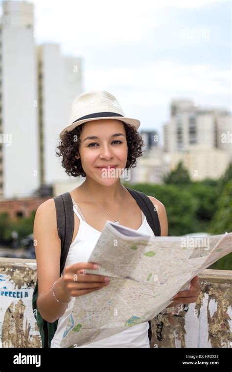 Female traveler holding city map, wearing white hat and casual clothes. Smiling and looking at ...