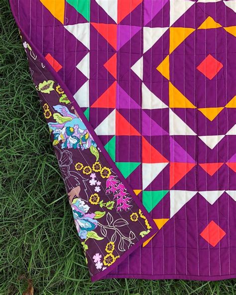 a quilt is laying on the grass with it's purple and orange color scheme