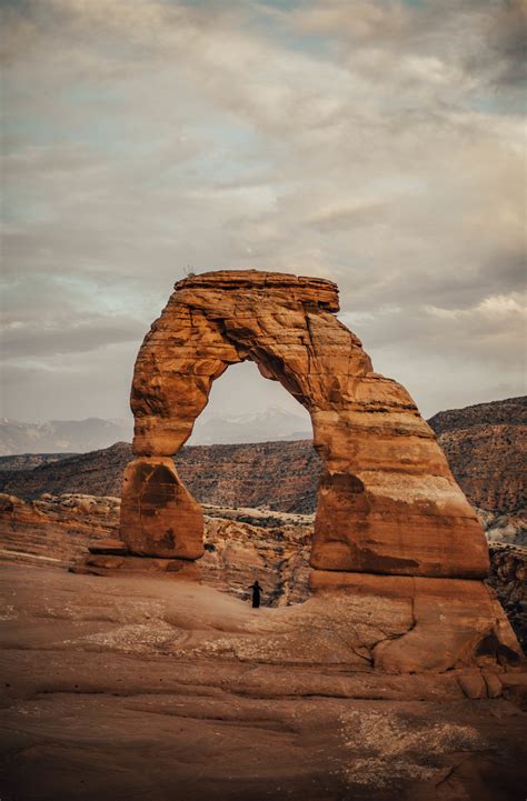 a person standing in front of an arch shaped rock formation on the side ...