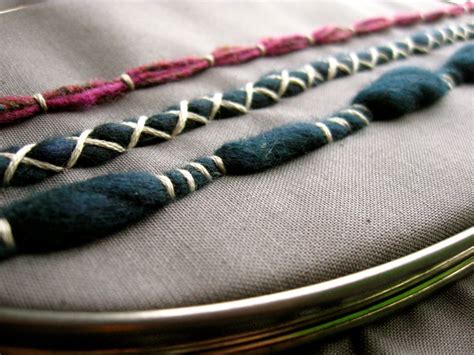several different colored beads are on a piece of fabric in a circular frame with a needle and ...