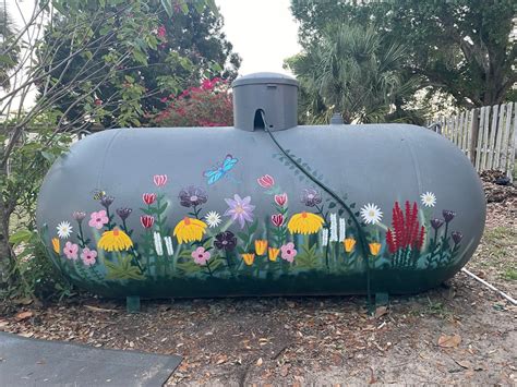 a large tank with flowers painted on it in the middle of a yard next to trees