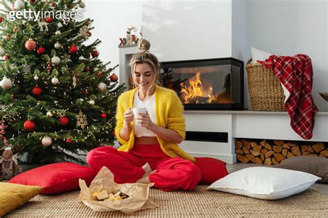 Happy woman sits beside a glowing fireplace in a cozy living room ...