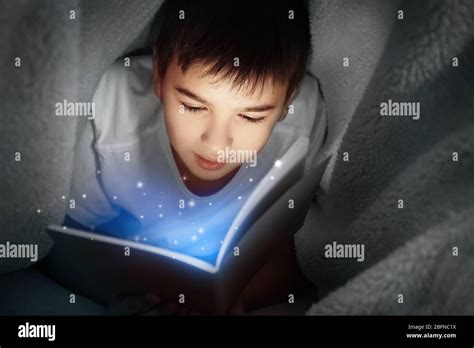 Cute boy reading book under blanket at night. Magic light coming out of book Stock Photo - Alamy