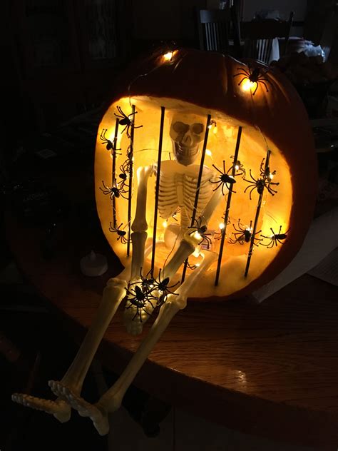 Skeleton in jail carved pumpkin lit with battery operated LED spider lights. Painted s ...