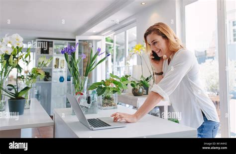 Female florist standing at her flower shop counter using mobile phone ...