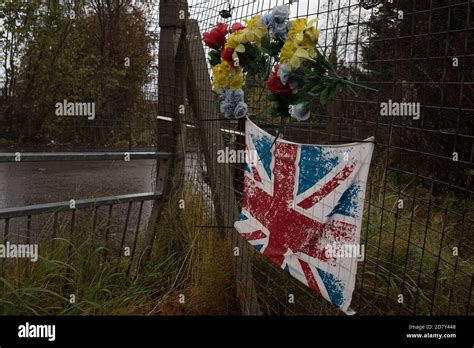 Union flag and plastic flowers in memory of young man, beside Thornliebank train station, in ...