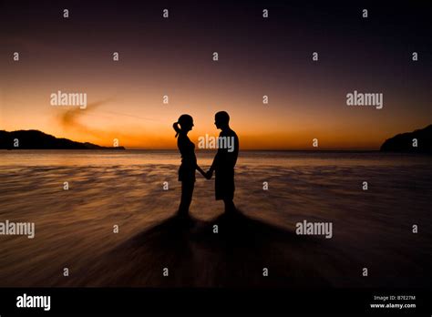 Silhouette of young couple holding hands on the beach and facing each ...