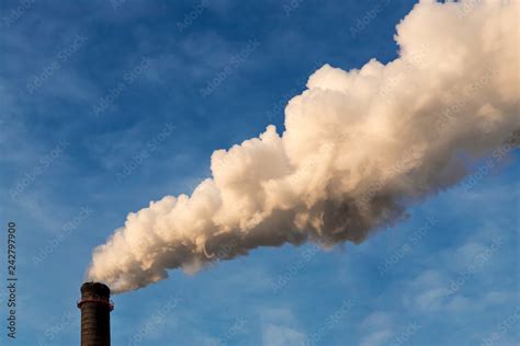 Heavy white smoke from an industrial chimney against a blue sky. Image of factory pollution with ...