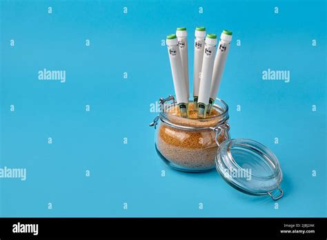 Glass jar with brown cane sugar and insulin syringe pens stuck into it on a blue background ...