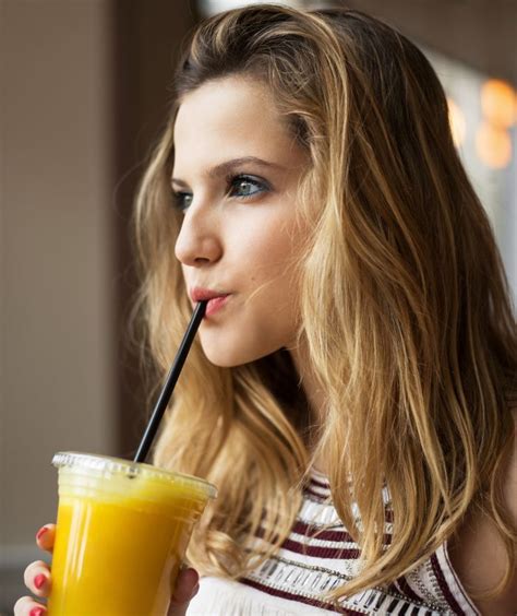 a beautiful young woman drinking orange juice with a straw in her mouth by luma studio for ...