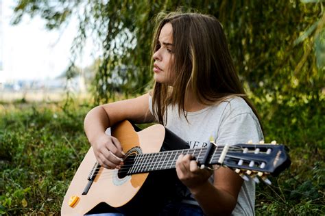 a young dark haired woman playing acoustic guitar while sitting on grass, outdoor acoustic ...