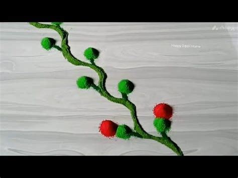 a flower made out of yarn sitting on top of a white sheet covered ground with red and green pom poms