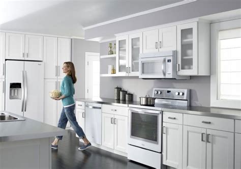a woman walking through a kitchen with white cabinets