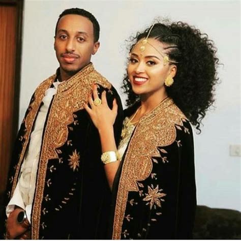 a man standing next to a woman in a black dress and gold jewelry on her ...