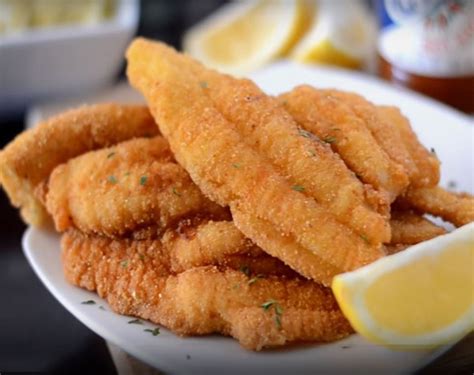 some fried food on a white plate with lemon wedges