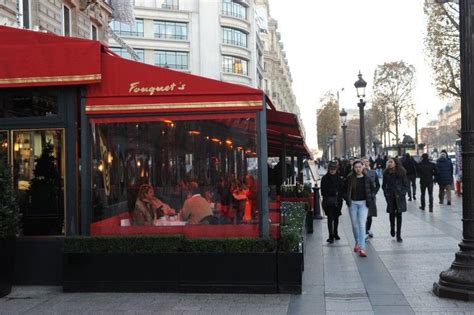 people are walking down the sidewalk in front of a red awning on a city street