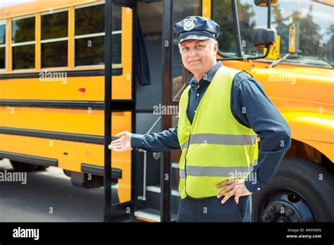 Senior driver weaering uniform standing near school bus showing door looking camera smiling ...