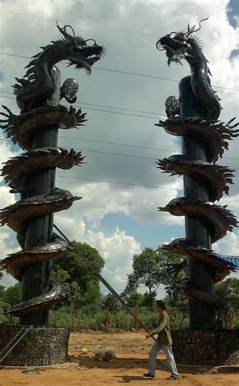 a man walking past two dragon sculptures on top of a dirt field with ...